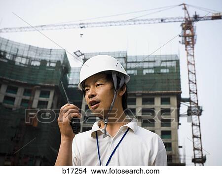 Man with construction helmet and crane in background holding walkie talkie View Large Photo Image Picture - Man with construction helmet and crane in background holding walkie talkie. Fotosearch