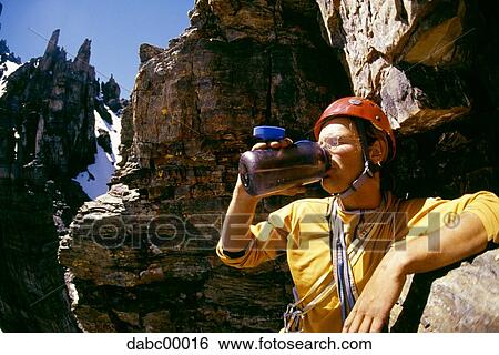 Man with helmet resting on rock and drinking water from bottle View Large Photo Image Stock Photograph - Man with helmet resting on rock and drinking water from bottle. Fotosearch