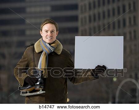 Stock Photo - Man with skates holding blank sign outdoors in winter. Fotosearch