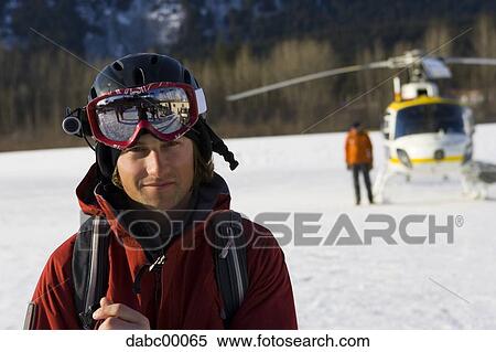 Man with ski goggles and helmet with helicopter and person in background View Large Photo Image Stock Photography - Man with ski goggles and helmet with helicopter and person in background. Fotosearch