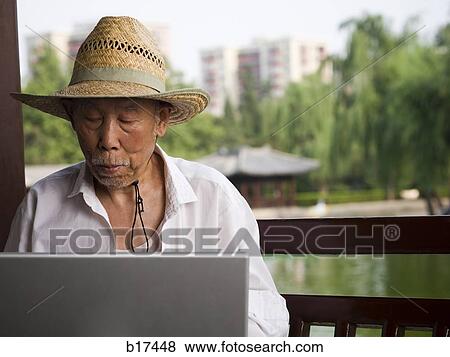 Stock Photo - Mature man with straw hat and laptop outdoors. Fotosearch