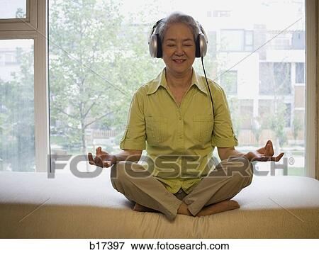 Mature woman sitting cross legged meditating with headphones smiling View Large Photo Image Stock Photo - Mature woman sitting cross legged meditating with headphones smiling. Fotosearch