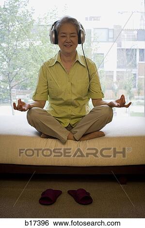 Mature woman sitting cross legged meditating with headphones smiling View Large Photo Image Stock Photograph - Mature woman sitting cross legged meditating with headphones smiling. Fotosearch