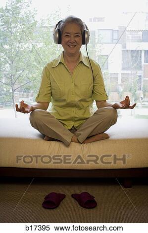 Mature woman sitting cross legged meditating with headphones smiling View Large Photo Image Stock Photography - Mature woman sitting cross legged meditating with headphones smiling. Fotosearch