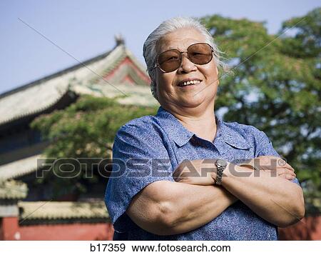 Mature woman standing outdoors with arms crossed smiling View Large Photo Image Stock Photo - Mature woman standing outdoors with arms crossed smiling. Fotosearch