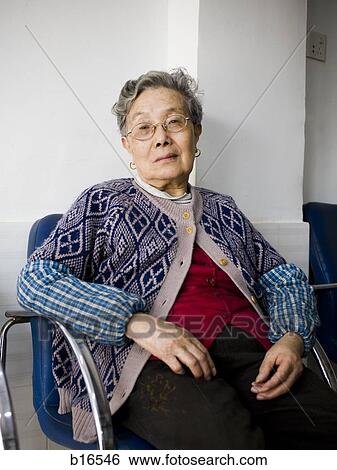 Stock Photograph - Mature woman with eyeglasses sitting in blue chair. Fotosearch