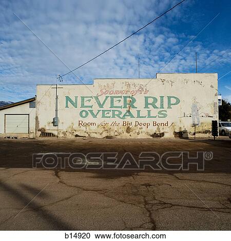 Stock Image - Old building with painted sign for Never Rip Overalls with parking lot and blue skies. Fotosearch