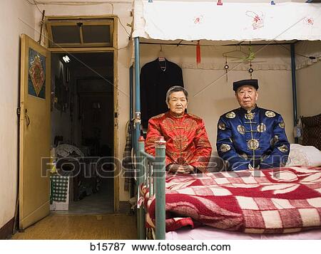 Stock Photo - Older couple sitting in room with bed. Fotosearch