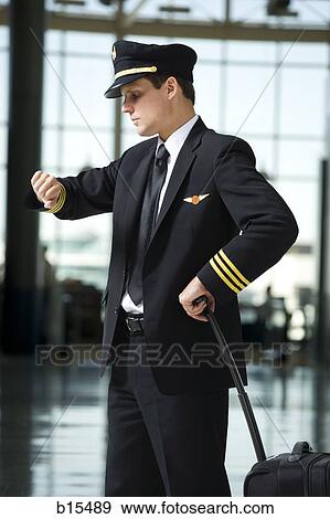 Pilot checking watch in airport with luggage View Large Photo Image Stock Photo - Pilot checking watch in airport with luggage. Fotosearch