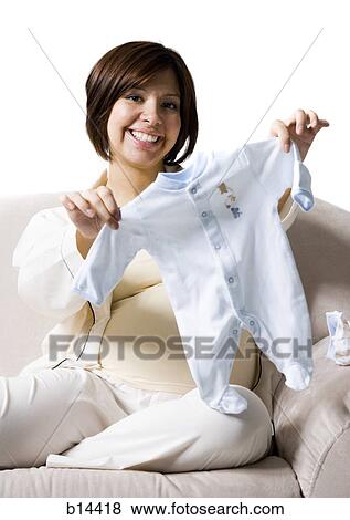 Stock Photo - Pregnant Woman holding baby clothing.. Fotosearch