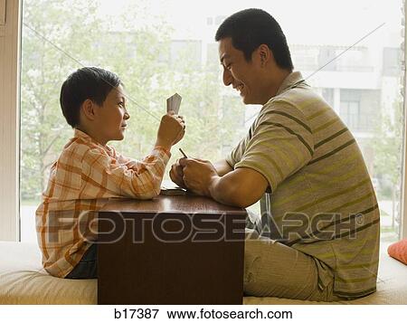 Profile of man and boy sitting cross legged in front of large window playing cards View Large Photo Image Stock Photo - Profile of man and boy sitting cross legged in front of large window playing cards. Fotosearch
