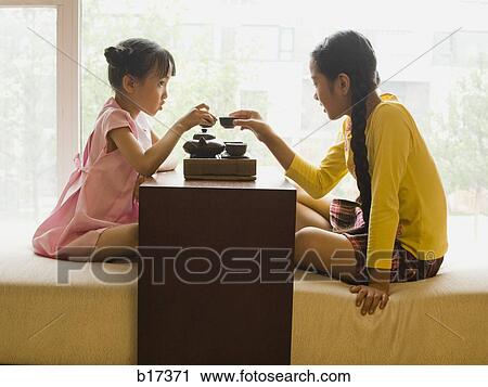 Stock Image - Profile of two girls sitting cross legged having tea. Fotosearch