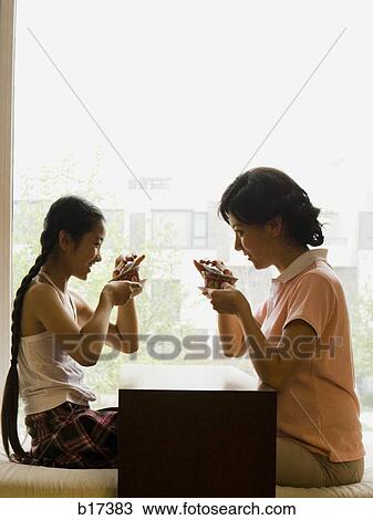 Stock Image - Profile of woman and girl sitting cross legged in front of large window. Fotosearch