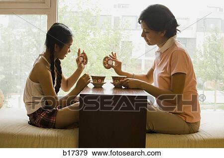 Stock Photo - Profile of woman and girl sitting cross legged in front of large window. Fotosearch