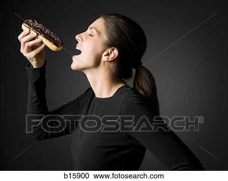 Stock Image - Profile of woman eating an? ©clair donut. Fotosearch