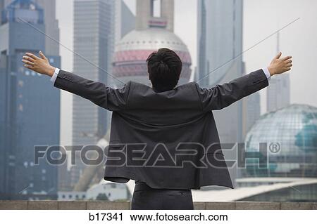 Rear view of businessman with arms up facing city skyline View Large Photo Image Stock Image - Rear view of businessman with arms up facing city skyline. Fotosearch