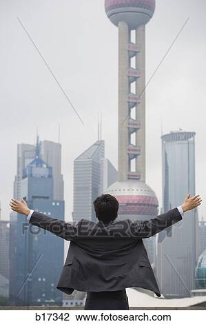 Rear view of businessman with arms up facing city skyline View Large Photo Image Stock Image - Rear view of businessman with arms up facing city skyline. Fotosearch