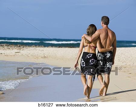 Rear view of couple walking on beach embracing View Large Photo Image Stock Photo - Rear view of couple walking on beach embracing. Fotosearch