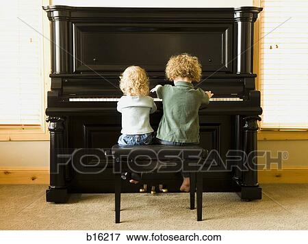 Rear view of two children sitting at upright piano View Large Photo Image Stock Photo - Rear view of two children sitting at upright piano. Fotosearch
