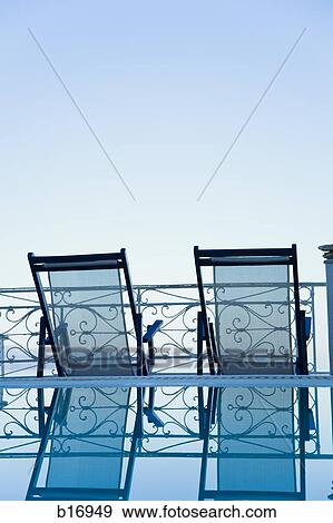 Rear view of two empty deck chairs and pool with reflection View Large Photo Image Stock Photo - Rear view of two empty deck chairs and pool with reflection. Fotosearch