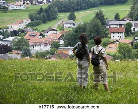 Stock Photography - Rear view of two women on hill with village below. Fotosearch