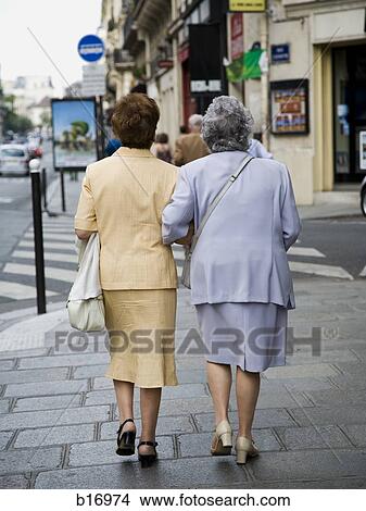 Rear view of two women walking on sidewalk outdoors View Large Photo Image Picture - Rear view of two women walking on sidewalk outdoors. Fotosearch