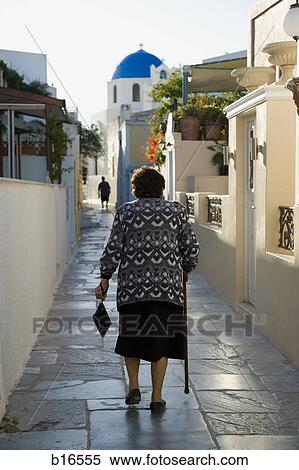 Stock Photography - Rear view of woman with cane walking on street in village. Fotosearch