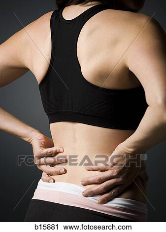 Stock Image - Rear view of woman with hands on lower back. Fotosearch