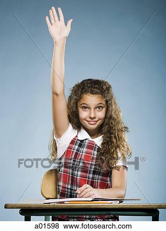 Stock Photo - Schoolgirl at desk with arm raised. Fotosearch