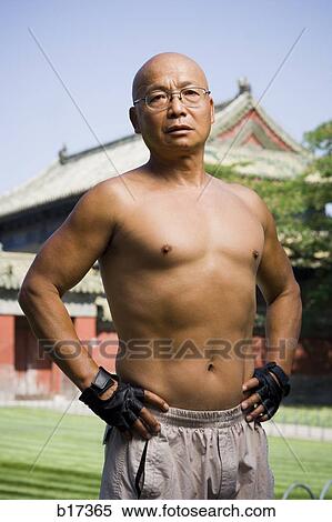 Stock Photography - Shirtless man standing outdoors with pagoda in background. Fotosearch