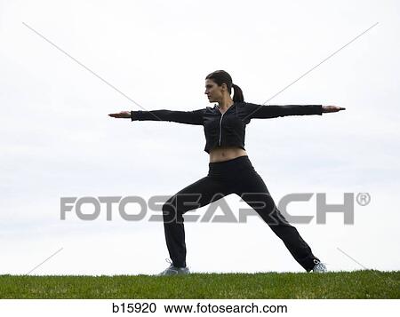 Stock Image - Side profile of woman stretching outdoors on grass. Fotosearch