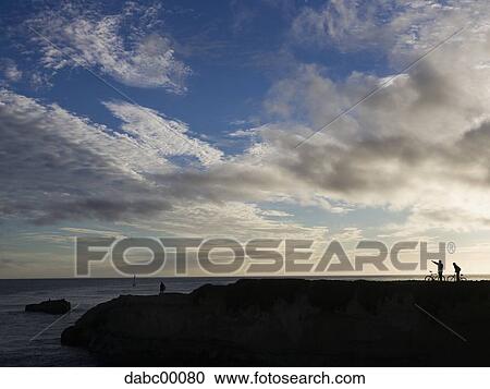Silhouette of people with bicycles on rock at water with blue sky and clouds View Large Photo Image Stock Image - Silhouette of people with bicycles on rock at water with blue sky and clouds. Fotosearch