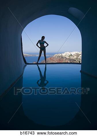 Silhouette of woman in bikini standing at edge of infinity pool with arch and rock formation View Large Photo Image Stock Image - Silhouette of woman in bikini standing at edge of infinity pool with arch and rock formation. Fotosearch