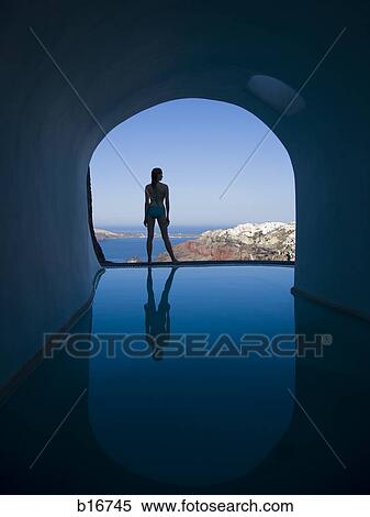 Silhouette rear view of woman in bikini standing at edge of infinity pool with arch and rock formation View Large Photo Image Stock Photography - Silhouette rear view of woman in bikini standing at edge of infinity pool with arch and rock formation. Fotosearch