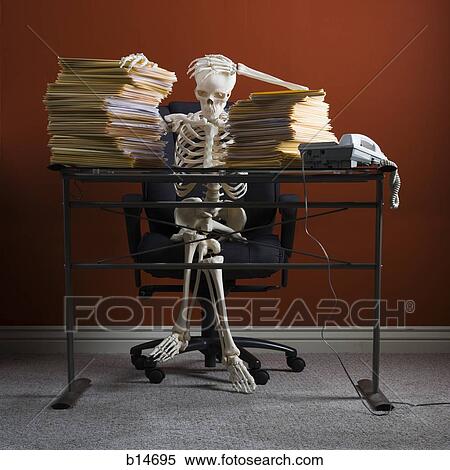 Skeleton Sitting At Desk With Stacks Of Paperwork Stock