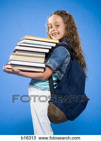 Stock Image - Smiling girl with backpack carrying pile of textbooks. Fotosearch