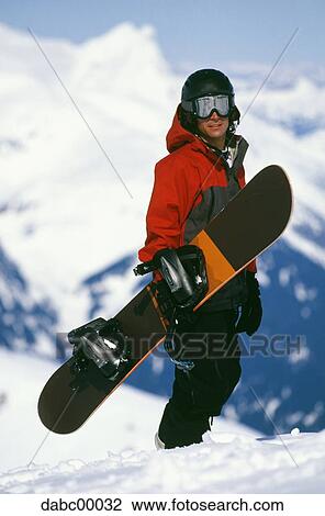 Snowboarder standing on mountain with snowboard View Large Photo Image Stock Image - Snowboarder standing on mountain with snowboard. Fotosearch