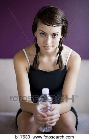Stock Image - Teenage girl sitting and holding bottled water smiling. Fotosearch