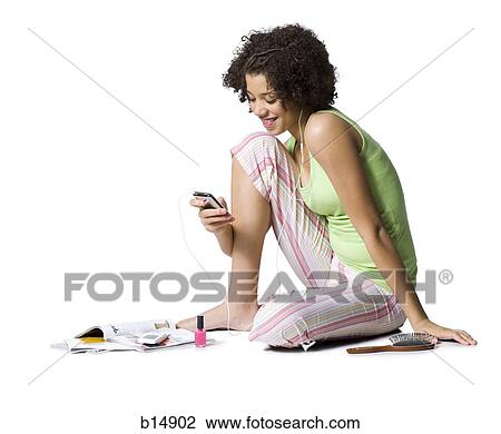 Stock Image - Teenage girl with MP3 player sitting and listening to music. Fotosearch