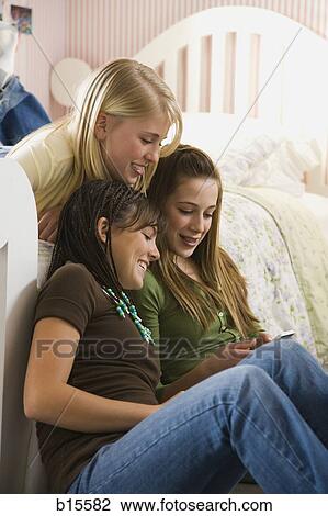 Stock Image - Three girls in bedroom with mp3 player. Fotosearch