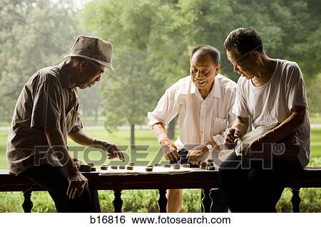 Stock Photograph - Three men playing board game outdoors smiling. Fotosearch