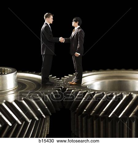 Two businessmen standing on cogs shaking hands View Large Photo Image Stock Image - Two businessmen standing on cogs shaking hands. Fotosearch