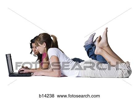 Two girls lying down looking at laptop View Large Photo Image Stock Photo - Two girls lying down looking at laptop. Fotosearch