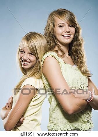 Two girls standing back to back smiling with arms crossed View Large Photo Image Stock Image - Two girls standing back to back smiling with arms crossed. Fotosearch
