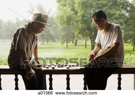 Two men sitting outdoors playing board game View Large Photo Image Stock Photograph - Two men sitting outdoors playing board game. Fotosearch