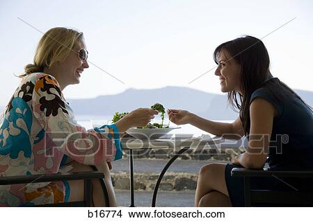 Two women eating salad outdoors and smiling with rock formation in background View Large Photo Image Picture - Two women eating salad outdoors and smiling with rock formation in background. Fotosearch