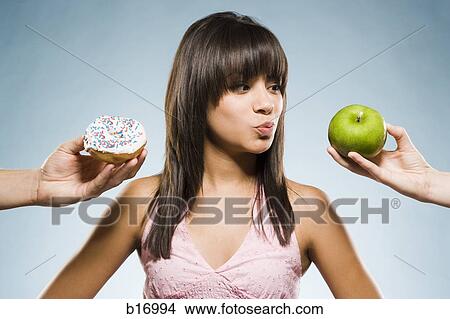 Woman deciding between a donut and green apple View Large Photo Image Picture - Woman deciding between a donut and green apple. Fotosearch