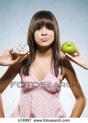 Stock Photo - Woman deciding between a donut and green apple. Fotosearch