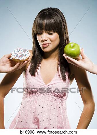 Stock Photo - Woman deciding between a donut and green apple. Fotosearch