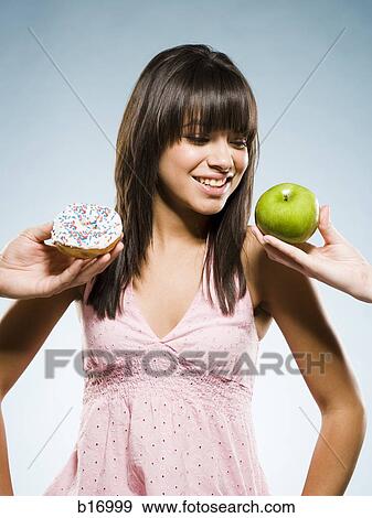 Stock Photo - Woman deciding between a donut and green apple. Fotosearch